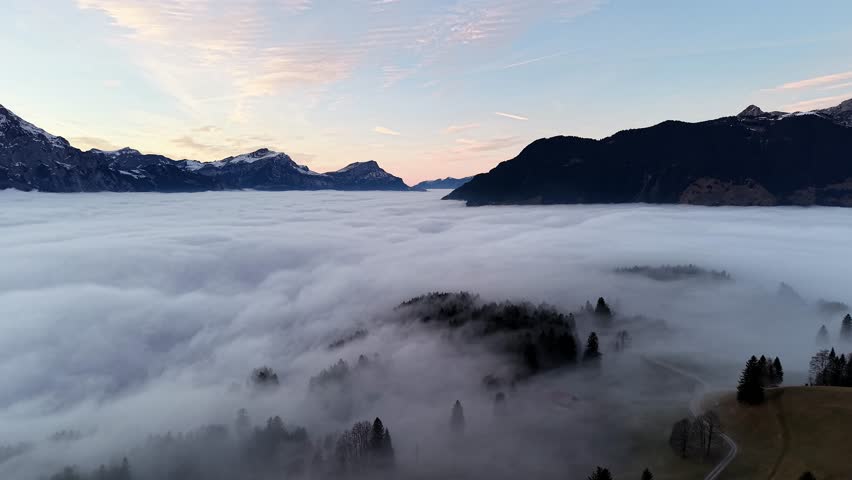 Wide aerial view showing a massive blanket of fog covering the valley below Haldi Schattdorf with mountain peaks rising through.