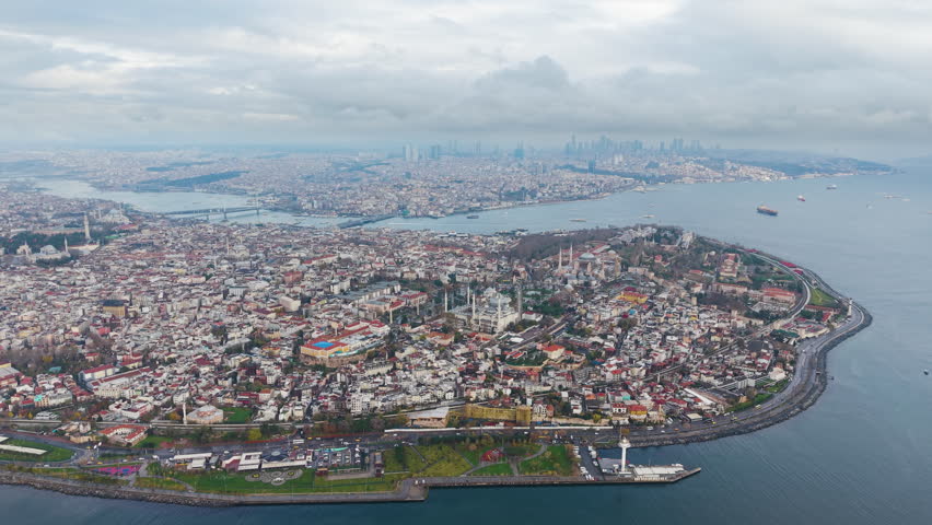 Wide drone shot of Istanbul’s Sultanahmet district showing dense historic buildings, mosques, and urban texture with the modern skyline in the distance. Cultural heritage and city life. UHD.