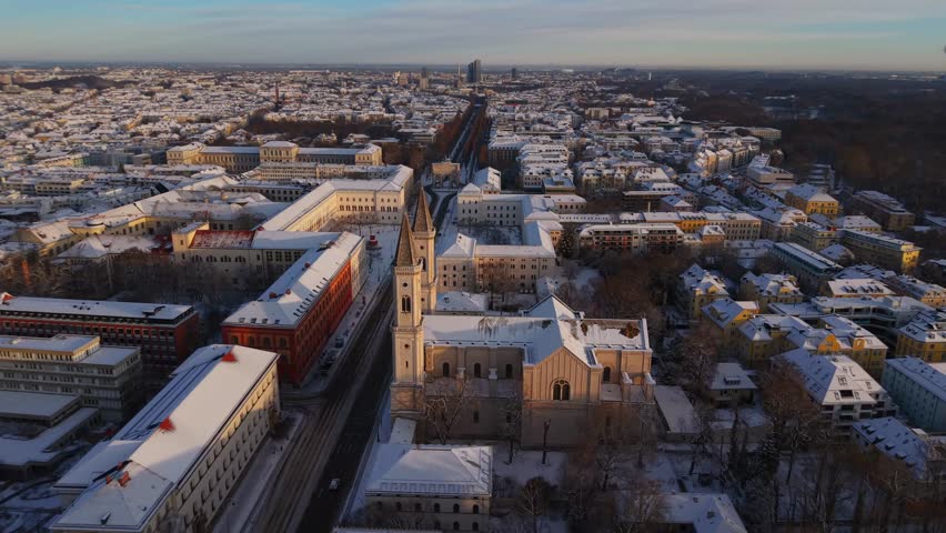 Aerial panorama of snowy Munich at sunrise, Bavaria, Germany. St. Ludwig Church with twin towers anchors Ludwigstrasse near LMU, calm winter morning in the historic city center. Luftaufnahme Muenchen