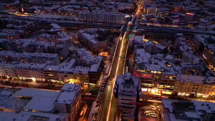 urban shopping street architecture and illuminated streets of Berlin Steglitz district covered in fresh snow during snowy winter evening. Unbelievable aerial view top down drone view