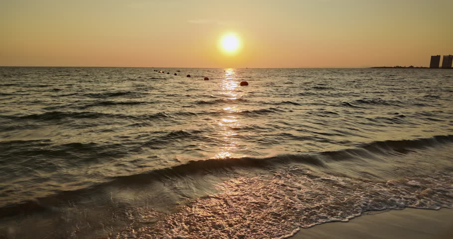 Golden sunset over a beach with waves breaking and a line of red buoys in the water. ( In slow motion)