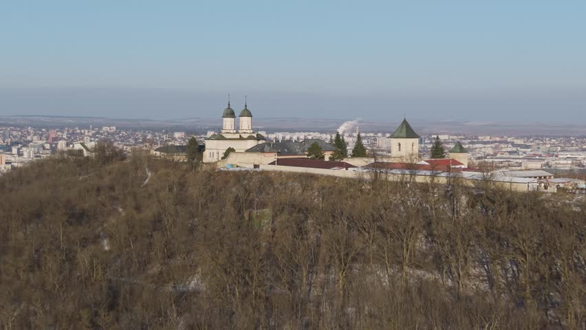 Aerial drone view of historic Cetățuia Monastery in Iași Romania with green domes overlooking snow-covered city rooftops and urban skyline