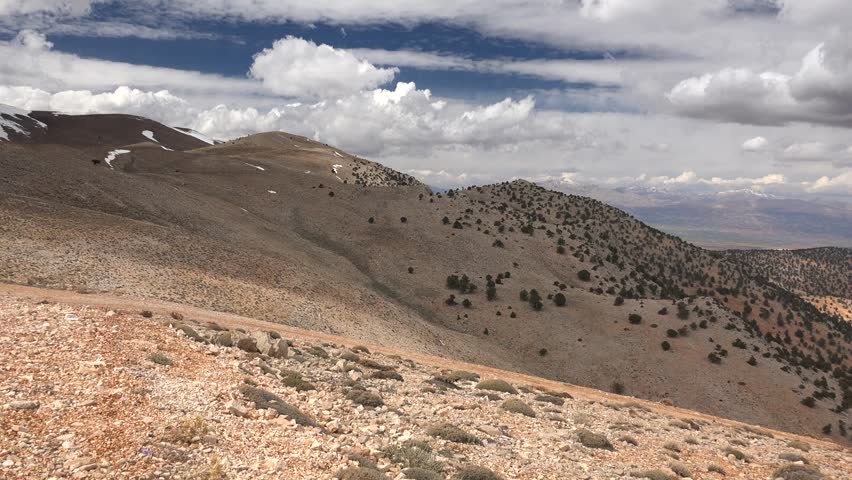 Panoramic semiarid mountain landscape with sparse trees under dramatic clouds Pakistan. Wide angle vista shows dry highlands and rugged ridges stretching toward distant horizons.