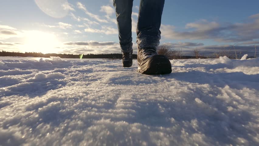 Close up of winter boots walking on snow in a sunny mountain area. Slow motion winter shot emphasizes cold climate, snowdrifts and outdoor activity in Canada.