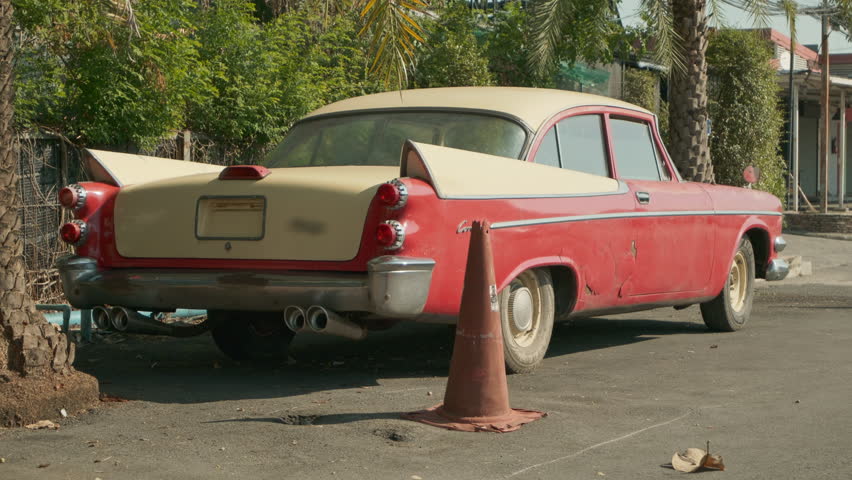 Close-up of the iconic tail fin and chrome bumper of a restored red American classic car parked on a sunny street.