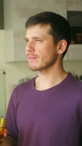 Gentle morning hydration, Man enjoying water peacefully, Man in purple shirt sips water during bright morning at home, Thoughtful man in purple shirt takes slow sip of water in natural kitchen light