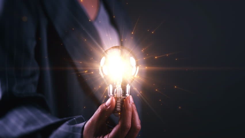 Innovation concept with a glowing light bulb held by a business professional on dark background, symbolizing creative ideas, inspiration, problem solving, leadership, strategy, and thinking business.