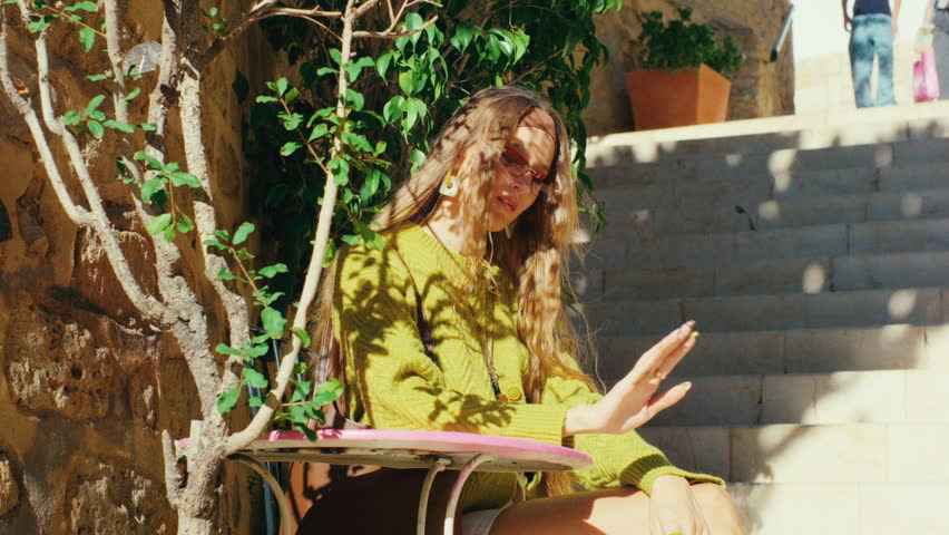 Young woman in sunglasses relaxing at sunny outdoor cafe