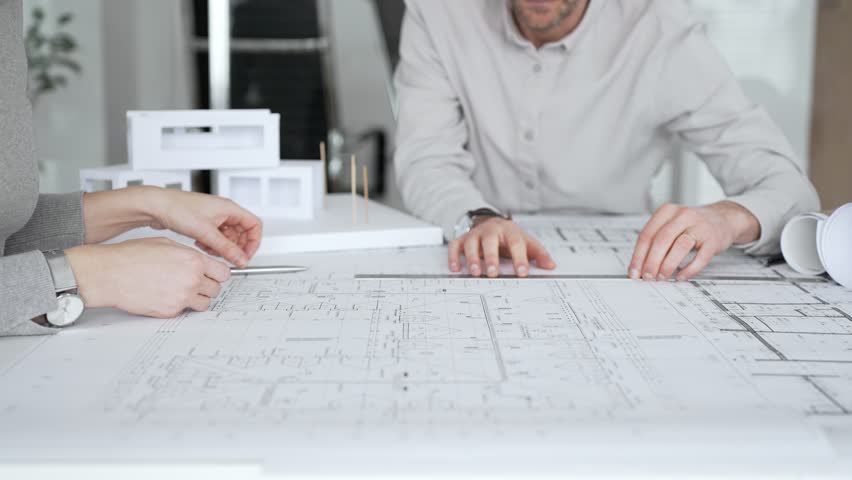 Architects are teamwork planning a building design project, reviewing detailed blueprints with a compass and a ruler, working on technical drawings and a digital tablet at the office, close up