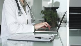 Healthcare female professional in white coat with stethoscope typing on laptop, managing patient records and telehealth data at desk. Medicine, health care and science concept - Powered by Shutterstock - Get 15% off with code: PIKWIZARD15