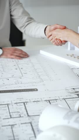 Handshaking between two architects finalizing a construction project deal, business partners agreeing on engineering blueprints and architectural models in an office, close up