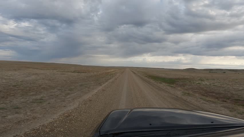 POV from a black truck moving forward on an isolated gravel road through a desert like landscape under a cloudy sky
