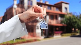 Graceful woman's hand holds silver house keys against the backdrop of a city townhouse. Real estate concept for the sale and purchase of houses and apartments. Real Time video. - Powered by Shutterstock - Get 15% off with code: PIKWIZARD15