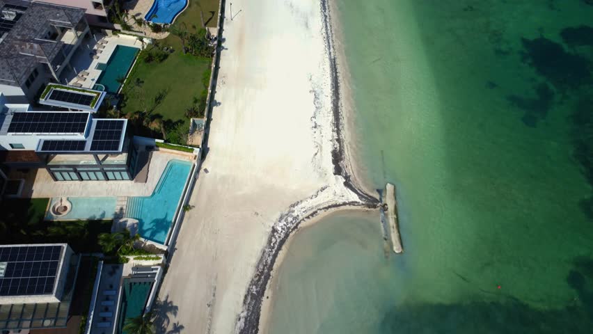 High-angle 4K top-down aerial drone shot of luxury beachfront resort pools and white sand beach coast line in Puerto Cancun, Mexico, featuring turquoise Caribbean waters and palm trees