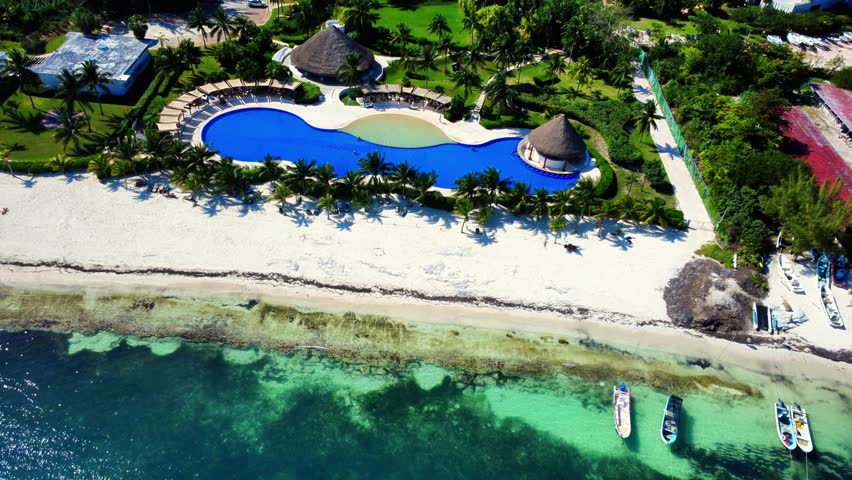 Aerial 4K drone shot of a luxury beachfront resort in Cancun, Mexico, featuring a blue infinity pool, white sand beach, turquoise Caribbean sea, and tall vacation apartment buildings