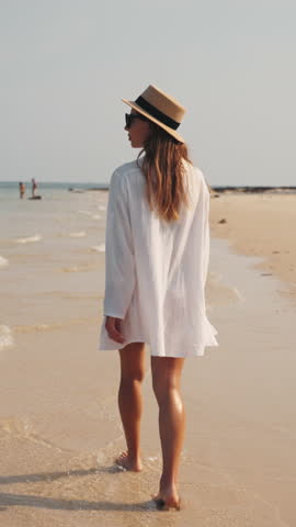Beautiful blonde woman in white shirt walking alone on amazing sandy beach in summer vacation, back view, slow motion. Travel and explore unique natural landmarks, feel happiness and joy, solitude