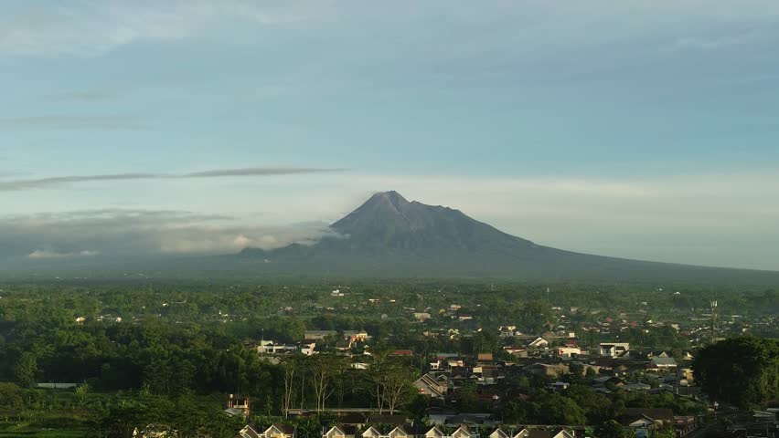 Aerial drone showing wide landscape view of a mountain rising above a green city area under clear sky