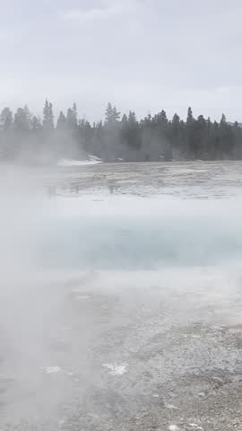 Steam rises from Opal Pool, a vibrant blue geothermal hot spring in Yellowstone National Park, showcasing active hydrothermal features and mineral-rich water in a volcanic landscape.