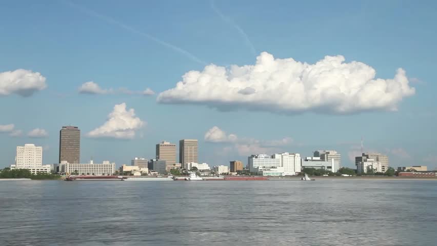 Scenic view of Mobile, Alabama skyline from the river on a partly cloudy day, showcasing urban waterfront, architecture, and peaceful river scenery.
