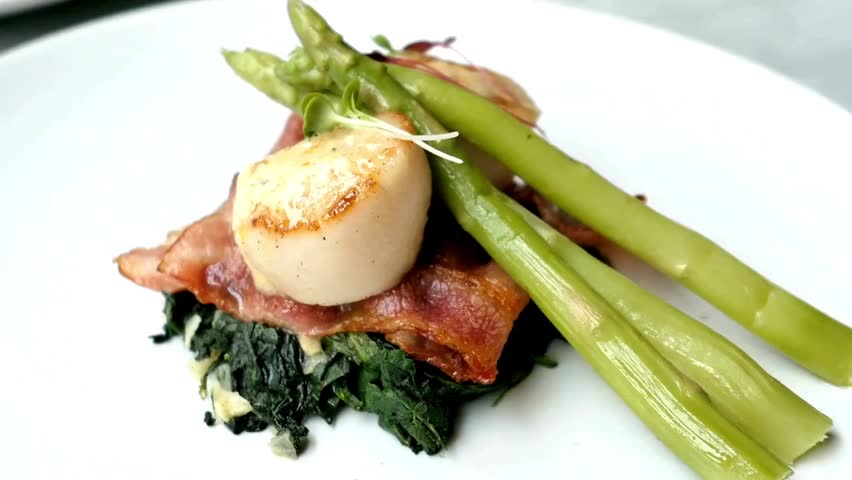 Pan-seared scallops served with crispy bacon, fresh spinach and asparagus, showcasing gourmet seafood cuisine, fine dining and elegant presentation.