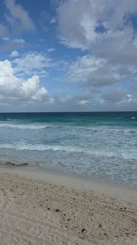 Sandy beach meeting clear ocean water under a partly cloudy sky, creating a calm and open coastal landscape.