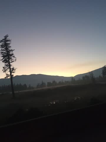 Soft dusk light over a quiet mountain landscape with silhouetted trees and rolling hills beneath a fading sky.