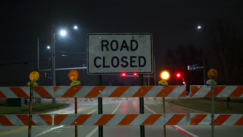 Road closed sign with illuminated construction barriers at night. traffic control, road maintenance, public safety infrastructure, nighttime construction work. POV view