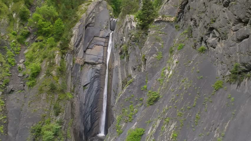 Aerial drone shot capturing the scenic Zruh Waterfall cascading down rugged rocks in the Eastern Caucasus mountains, Dagestan, Russia. The footage highlights the vibrant green forested ridges and natu