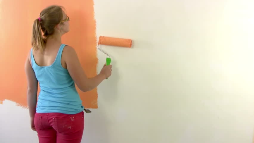 Girl paints a wall in orange with a paint roller. At the end, puts his signature