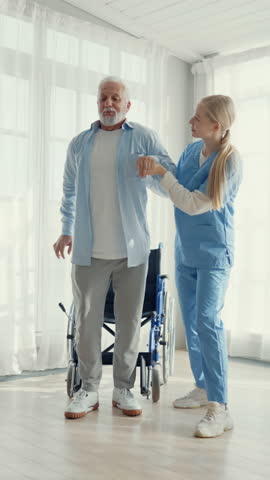 Rehabilitation after trauma or heart attack in hospital, nurse helping to old man to walk. Aged sick man trying to go after cerebral stroke, curing for disabled person in modern clinic, nursing house