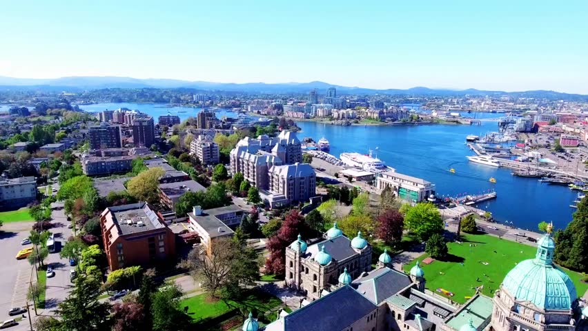 Tranquil aerial view captured on 12 June 2025 of Inner Harbour, Victoria, British Columbia, Canada. Downtown waterfront with calm reflective water, docked boats, greenery, and modern cityscape blending peaceful urban life with natural coastal beauty.
