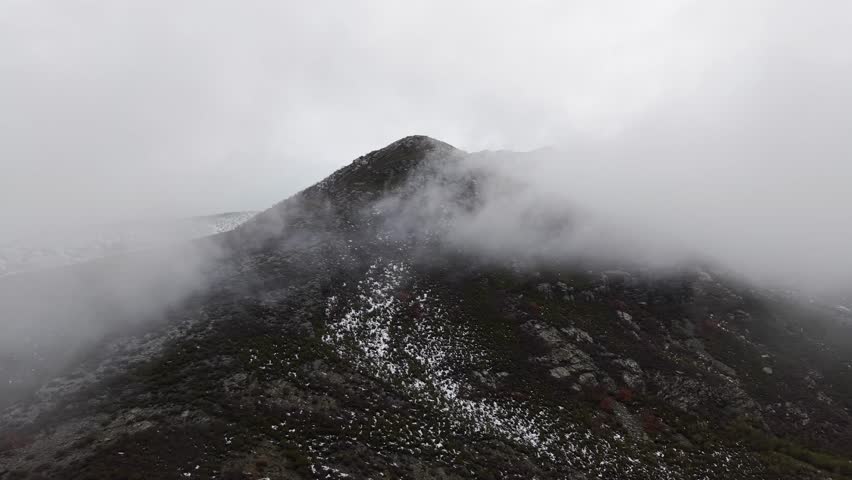 Aerial view of snowy mountain peak flying through the fog and clouds