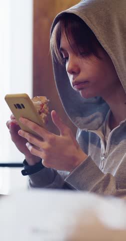 Slow motion vertical 4k footage of a teenage girl is consumed by social networks in a fast food cafe. Modern youth addictions are unhealthy tendencies that destroy physical and mental health.