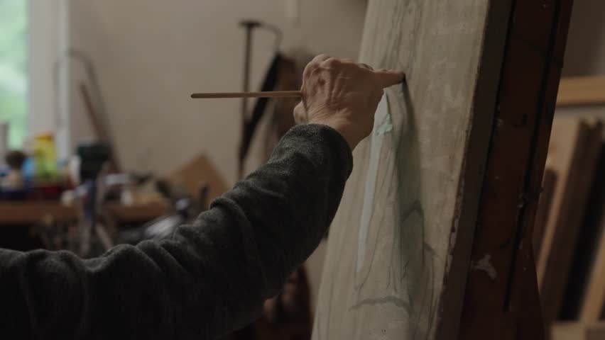 Senior artist on a wheelchair paints an oil painting on canvas in a studio