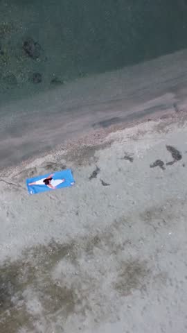 Vertical aerial drone shot of a woman doing Upward Facing Dog (Urdhva Mukha Svanasana) yoga pose on a serene beach