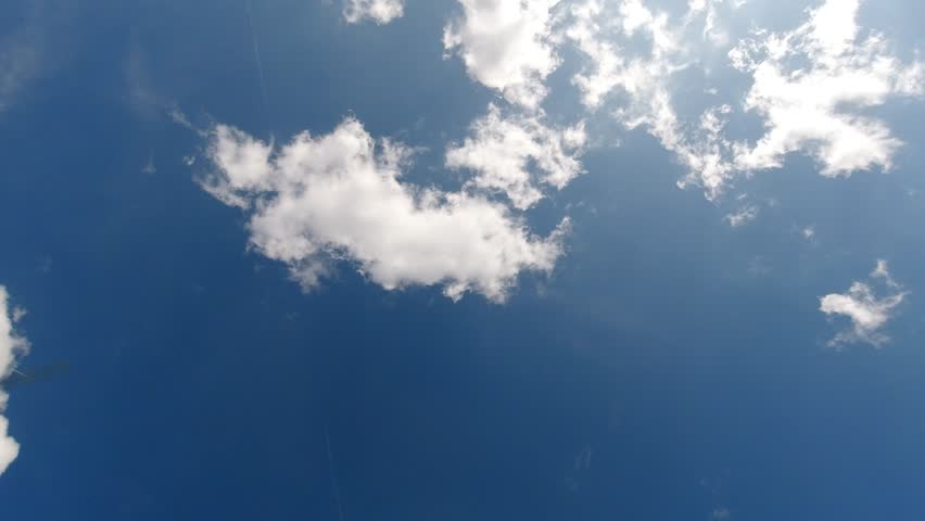 White clouds float across a deep blue sky as an airplane flies overhead, leaving a white contrail