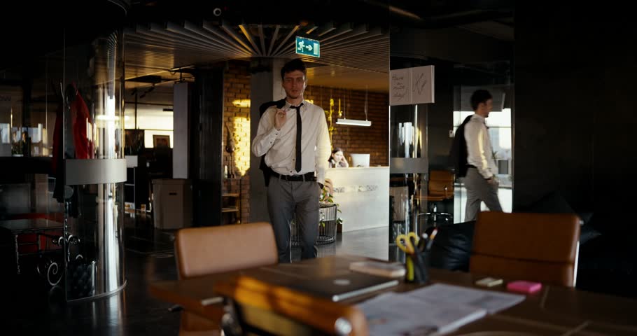 A young professional adjusts his attire, readying himself for an important meeting in a stylish office space