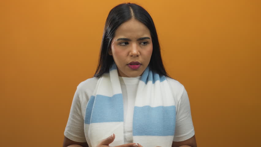 Woman holds up her fingers while counting in a soft background showcasing a young latin hispanic supporter wrapped in an orange scarf against an isolated wall.