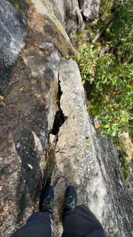 Hiker Carefully Moving Along High Ledge Above Forest on Jordan Cliffs Trail (Acadia National Park, Maine, USA)