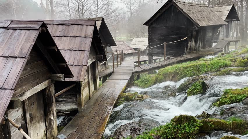 Traditional wooden watermills standing above a flowing river in Jajce, Bosnia and Herzegovina. Historic rural scene showing old craftsmanship, nature, and cultural heritage in a misty landscape