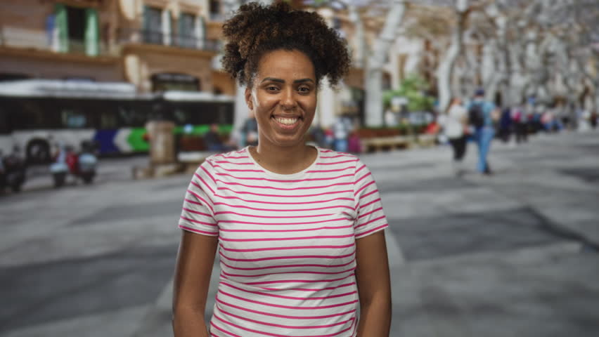 Young woman smiling and standing on a busy street in front of a coach bus and blurred pedestrians; urban resilience confidence.