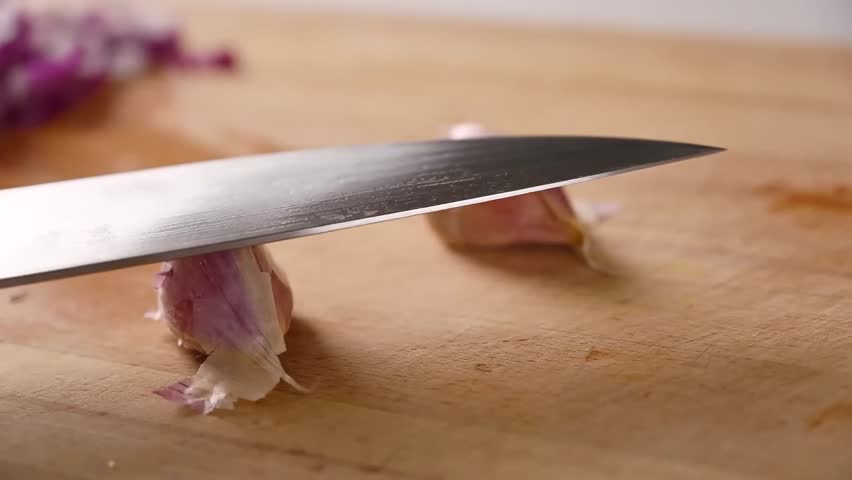 Slicing fresh garlic cloves on a wooden surface