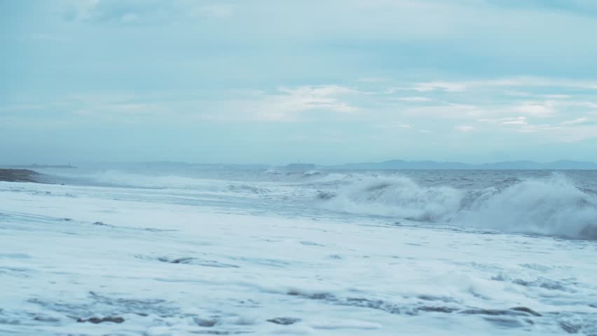 Beneath a cloudy sky, powerful waves crash against the shores of Shonan Beach in Kanagawa, Japan.