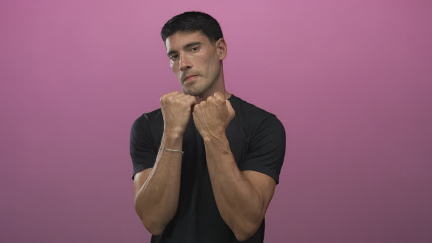 Hispanic man wearing black tshirt with clenched fists punching against pink wall in studio; discipline determination.