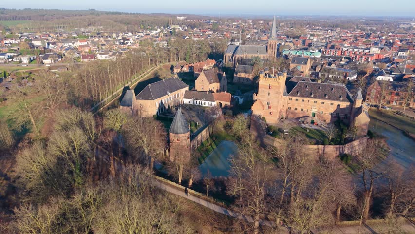Aerial view of Dutch town red brick castle with moat, church spire, dense homes, and distant wind turbines blend medieval heritage with modern sustainability.