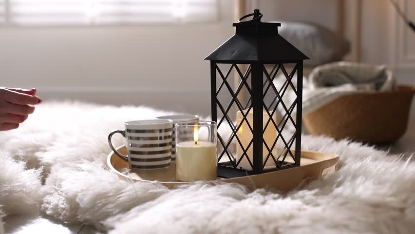 Woman taking cup of hot drink from tray with beautiful Christmas lantern and burning candles indoors. Camera moving forward