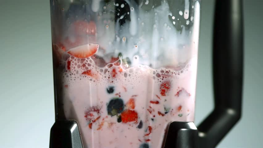 Close Up of a Blender Mixing a Pink Berry Smoothie with Sliced Strawberries and Whole Blueberries Swirling in Slow Motion against a Grey Background