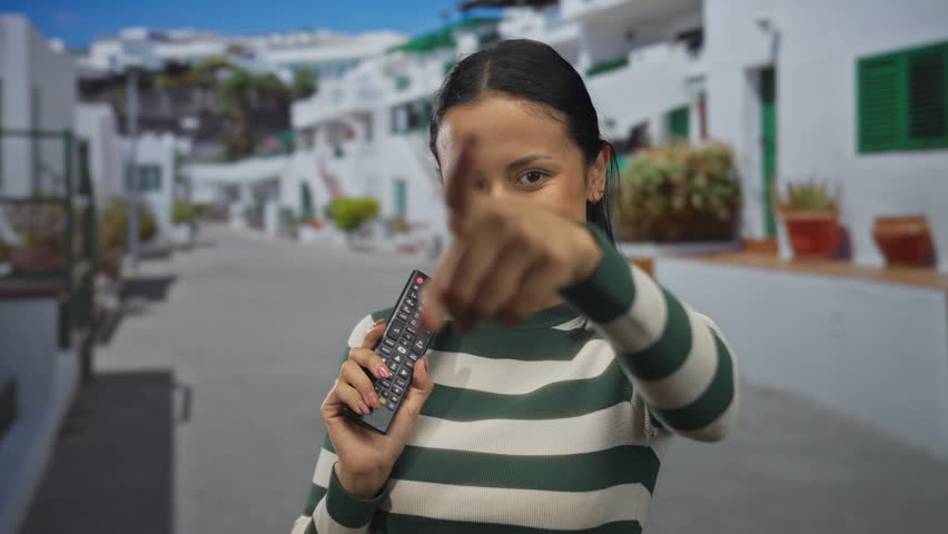 Woman smiling while holding a television remote on a vibrant street, showcasing hispanic culture in an outdoor setting, reflecting joy and leisure.