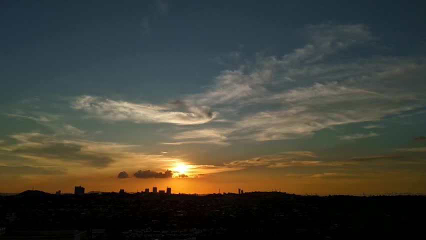 Time lapse of a city skyline at sunset showing shifting clouds glowing skies and changing light as buildings silhouette against warm colors and evening atmosphere