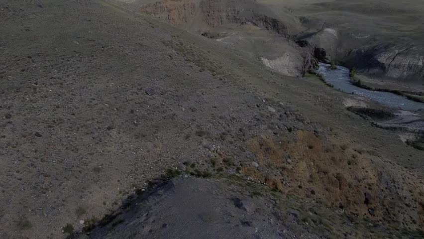 Rocky hillside with a river running through it. The sky is dark and the landscape is desolate